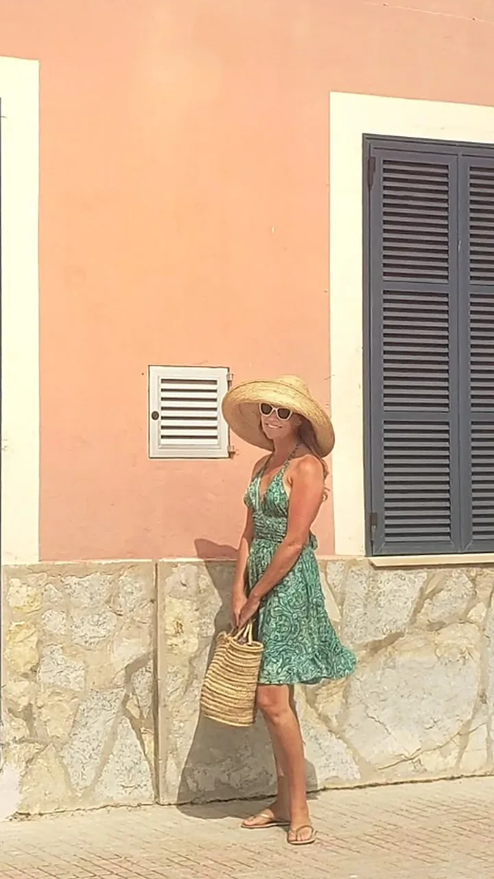 Rayne in a green dress against a pink village wall